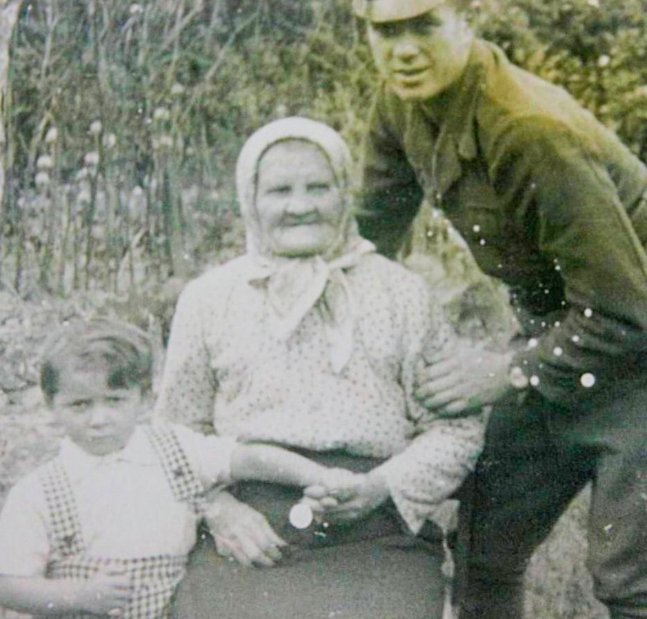 Stara, rodzinna fotografia trzech pokoleń: starsza kobieta w chuście, mężczyzna w mundurze wojskowym i młody chłopiec. Idealna ilustracja do artykułu o zapomnianych nazwach relacji rodzinnych i stopniach pokrewieństwa na blogu Tradicon.